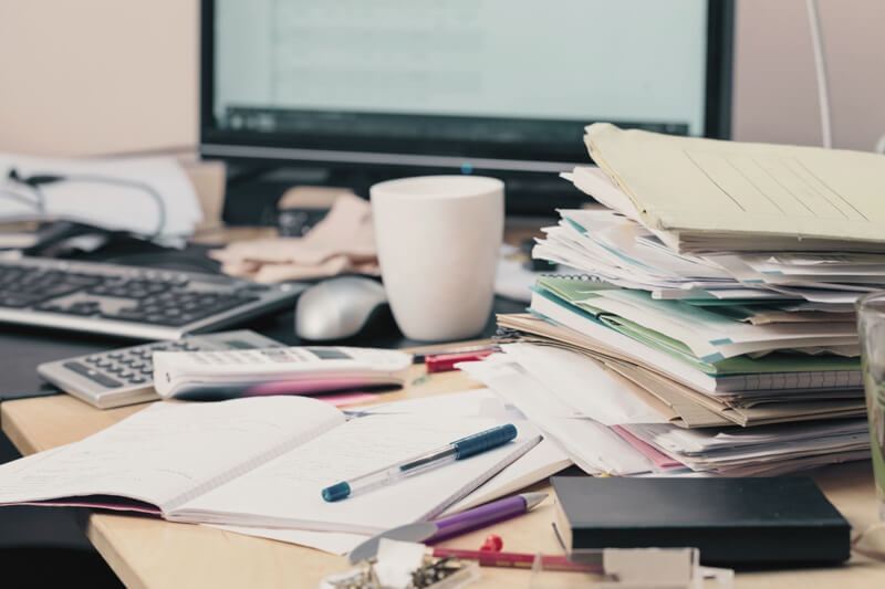 A cluttered desk with papers and documents scattered around. Small business owners may face challenges when preparing their BAS due to the complexity of the Australian tax system, record-keeping difficulties, and the importance of accurate classification of financial transactions.